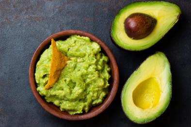 a tortilla chip is stuck in a bowl of guacamole next to two avocado halves