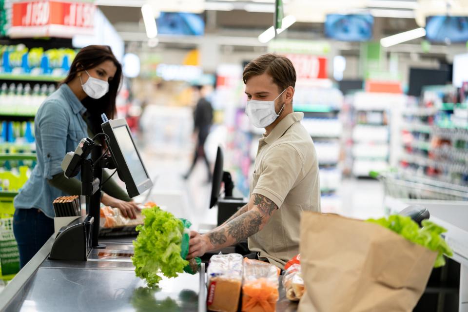 a supermarket cashier scans a woman's groceries while both wear protective face masks