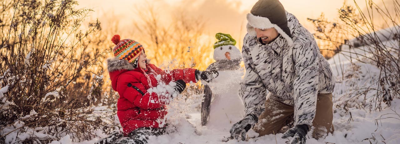 Photo of little boy building a snowman with his dad.