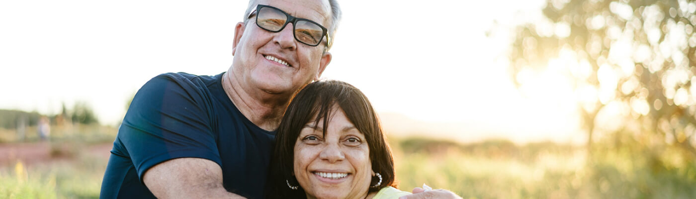 A man and woman embrace each other in the outdoors as the sun goes down