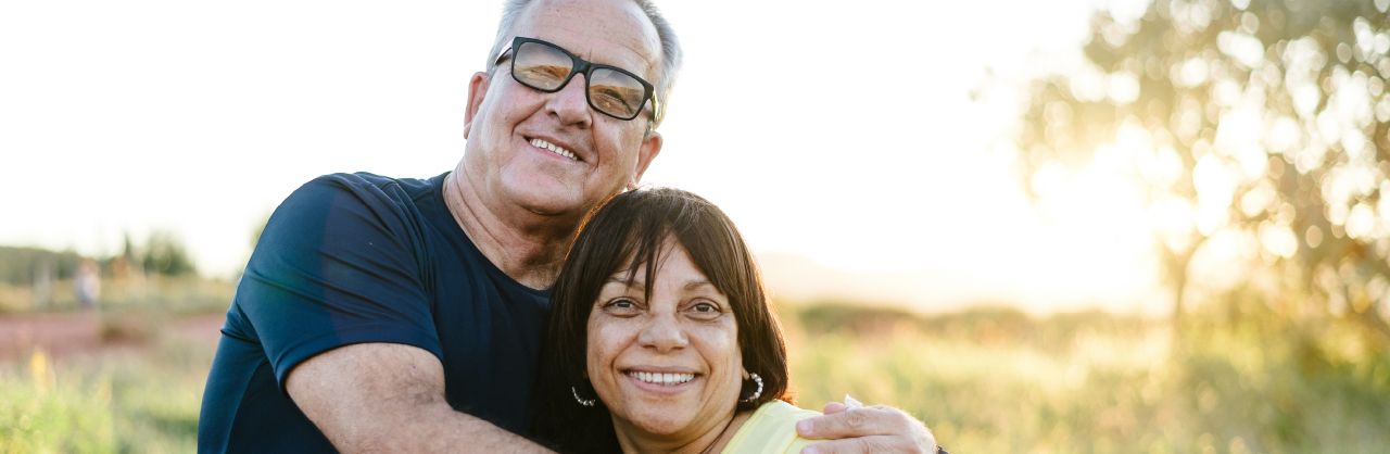 A man and woman embrace each other in the outdoors as the sun goes down