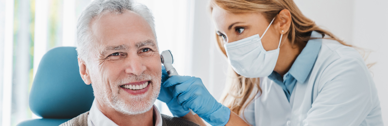 a physician checks a man's ear with her otoscope