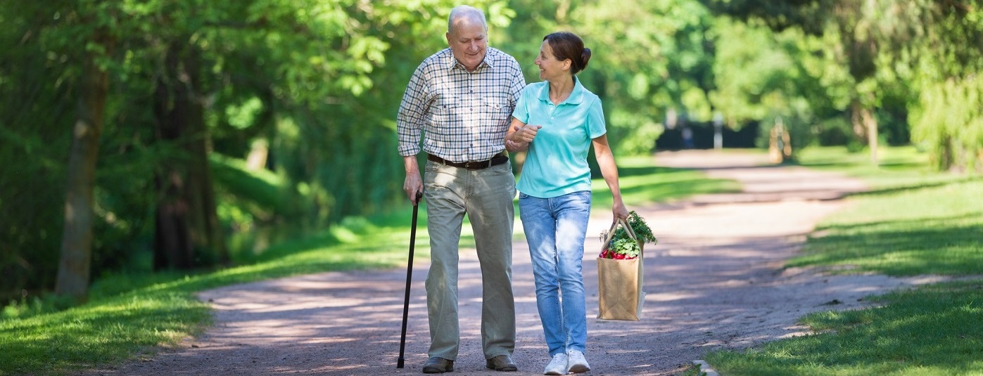 Elderly man using cane and walking with woman.
