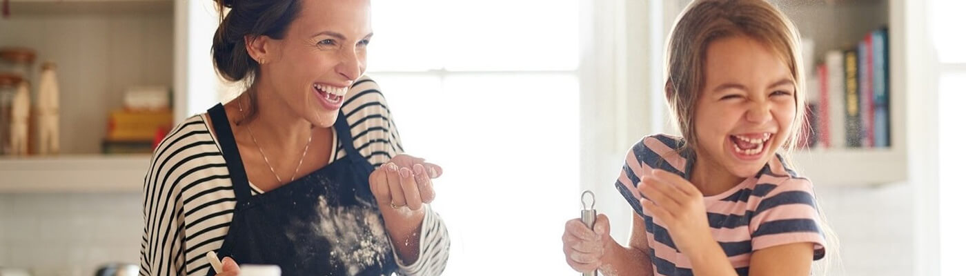 Photo of laughing mom and young daughter cooking.