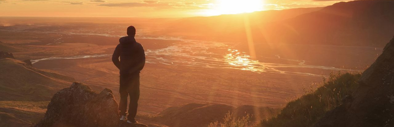 a hiker viewing a sunset over a great valley in the mountains 