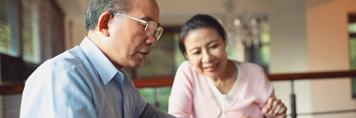 Man checking his blood pressure at home with his wife looking on.