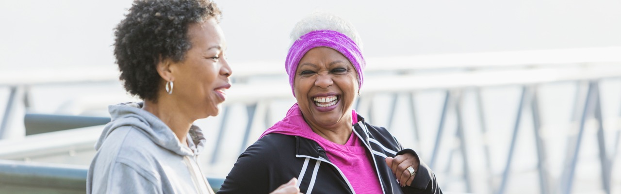 Two older women are jogging in front of a bridge
