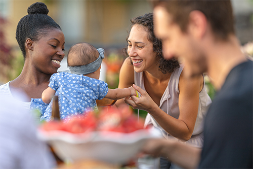 a mother introduces her newborn to a friend while at an outdoor picnic