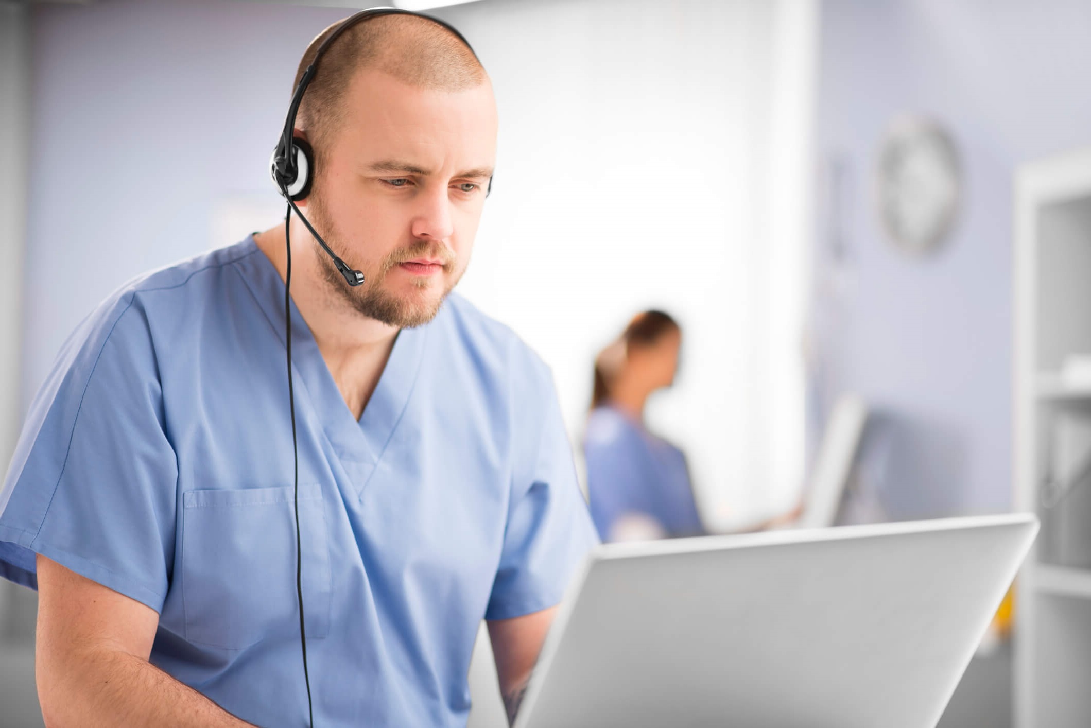 Male nurse on phone and computer, talking with patient.