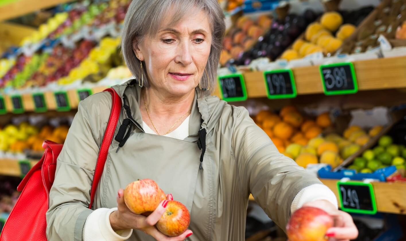Woman shopping for food in produce section of grocery store.