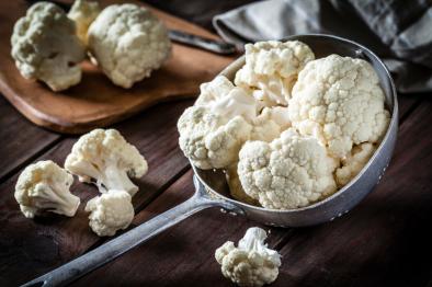raw cauliflower in a metal cooking spoon resting on a wooden table