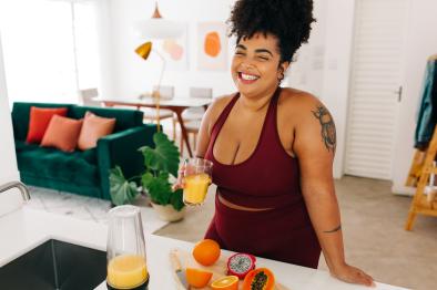 Photo of smiling, young woman drinking a glass of freshly-made juice.