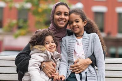 Photo of muslim mother hugging daughters in city park