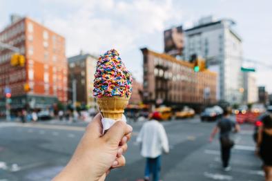 Photo of someone holding ice cream cone with downtown behind