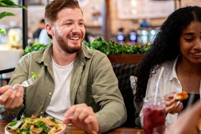 Photo of young man eating healthy food at restaurant with friends.