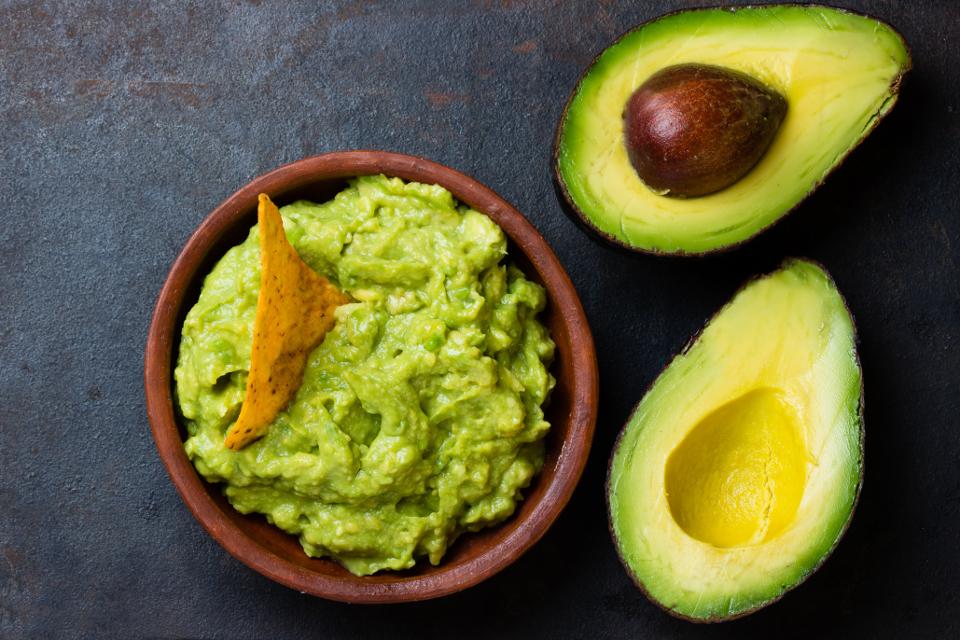 a tortilla chip is stuck in a bowl of guacamole next to two avocado halves