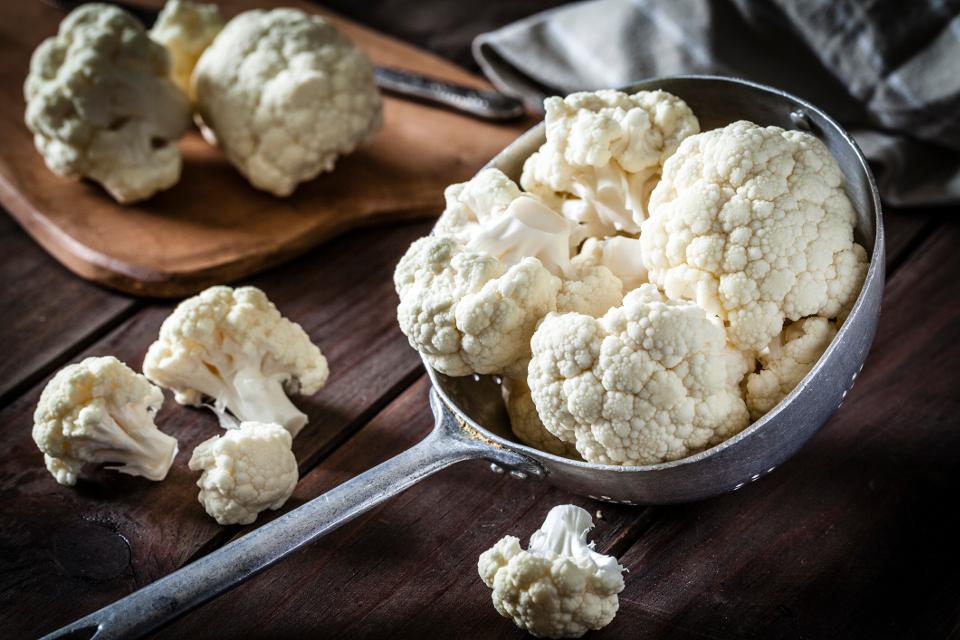 raw cauliflower in a metal cooking spoon resting on a wooden table