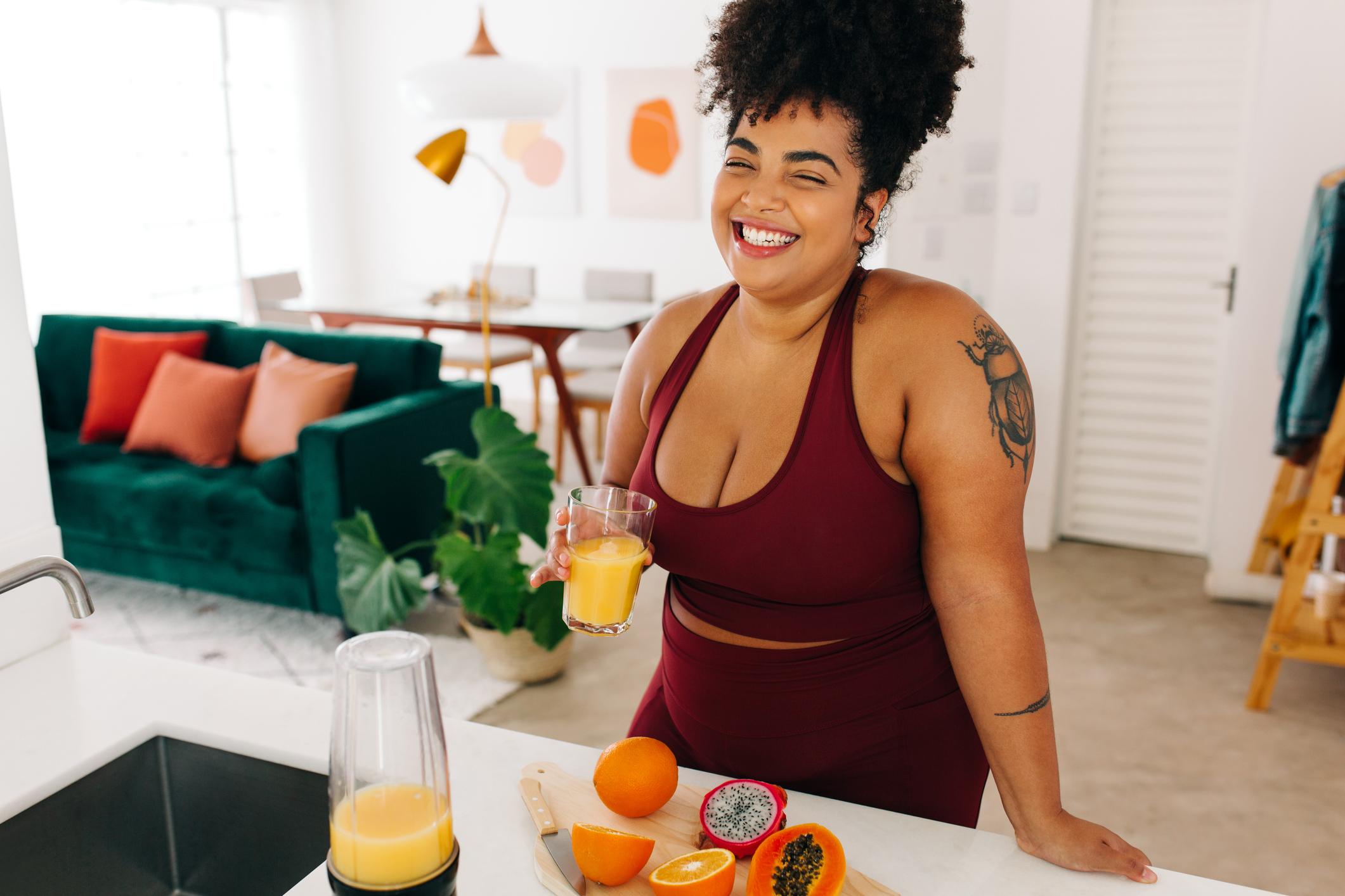 Photo of smiling, young woman drinking a glass of freshly-made juice.