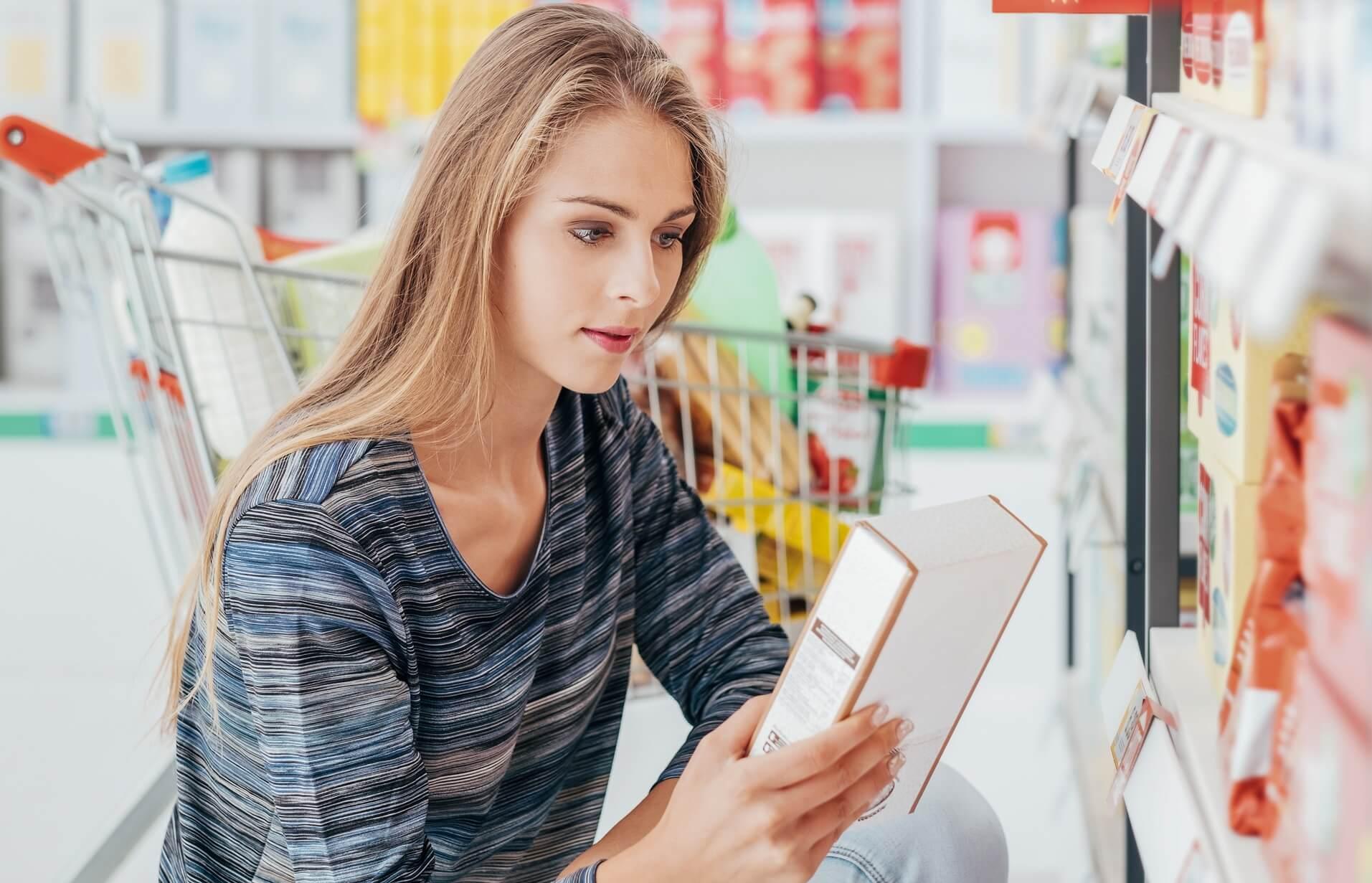 Photo of young woman reading food nutrition label.