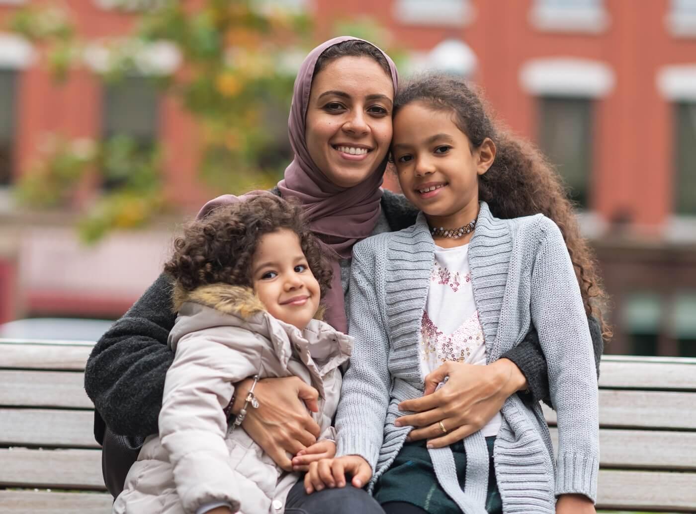 Photo of muslim mother hugging daughters in city park