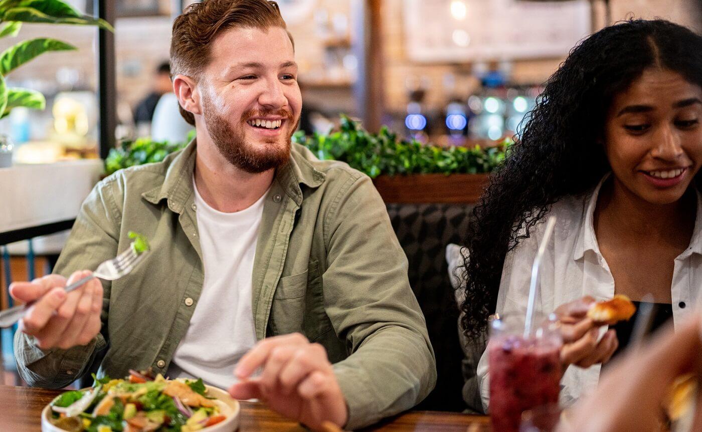 Photo of young man eating healthy food at restaurant with friends.